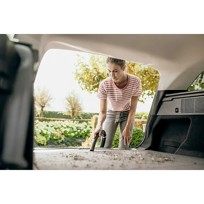 Kärcher Elektro-Nass- & Trockensauger WD 4 S GO!Further - 1.100 W, Behältervolumen: 20 l - Frau saugt den Kofferraum eines Autos mit einem Kärcher-Staubsauger. Das Auto steht im Freien mit Bäumen im Hintergrund.