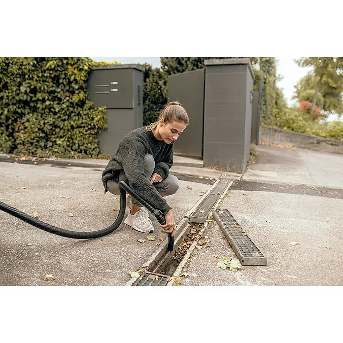 Kärcher Elektro-Nass- & Trockensauger WD 4 S GO!Further - 1.100 W, Behältervolumen: 20 l - Eine Frau reinigt einen Abfluss mit einem Staubsauger, um ihn von Blättern zu befreien. Der Fokus liegt auf dem Staubsauger und dem sauberen Abfluss.