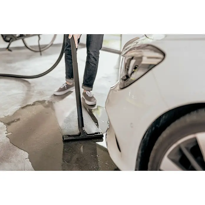 Kärcher Elektro-Nass- & Trockensauger WD 4 S GO!Further - 1.100 W, Behältervolumen: 20 l - Ein Mann reinigt mit einem Nasssauger Wasser neben einem weißen Auto in einer Garage, um Sauberkeit und Trockenheit zu gewährleisten.