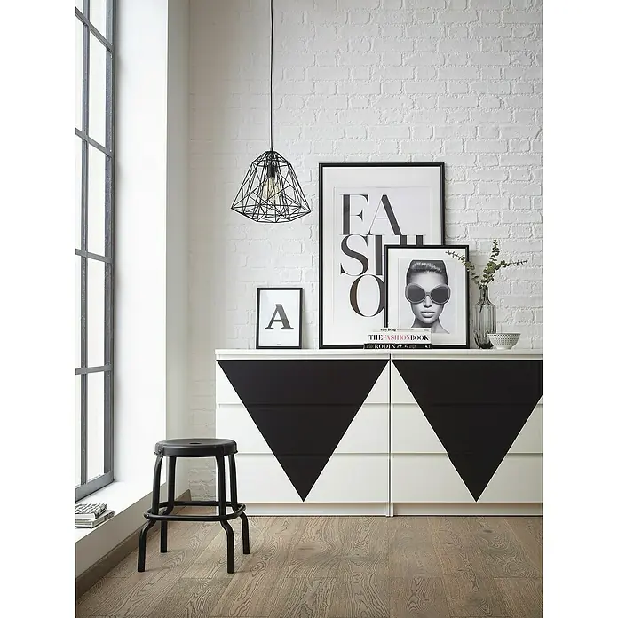 D-c-fix Klebefolie Uni Seidenmatt - 200 x 45 cm, Schwarz, Selbstklebend - Dekorative Einrichtung mit einem schwarzen Hocker und einer Kommode mit Dreiecksmuster vor einer weißen Ziegelwand.
