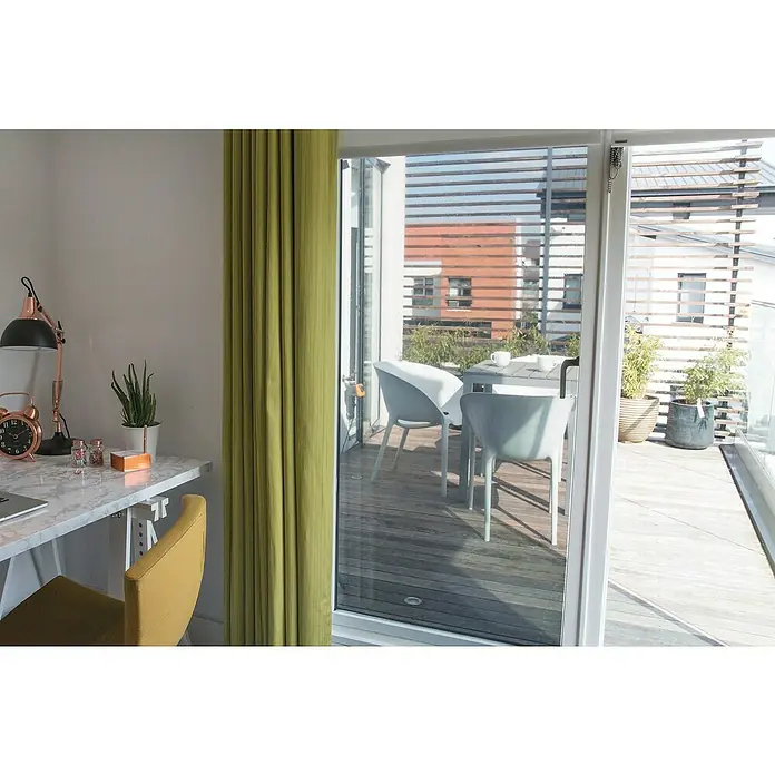 D-c-fix Tönungsfolie - 200 x 90 cm, Mit UV-Schutz, Statisch haftend - Einblick in ein stilvolles Heimbüro mit einem Schreibtisch, einer goldenen Lampe und grünen Vorhängen mit Zugang zu einem Balkon.