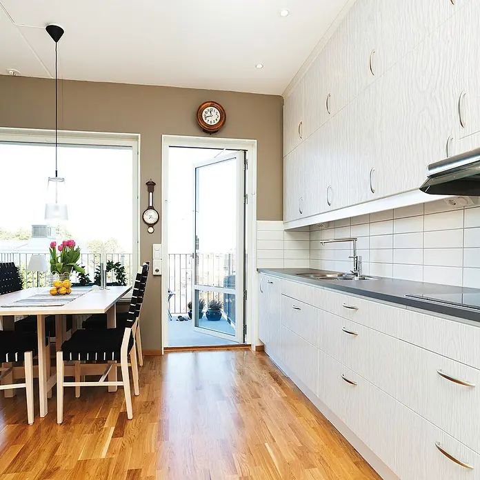 D-c-fix Holzoptikfolie Whitewood - 200 x 67,5 cm, Weiß, Selbstklebend - Ein helles Esszimmer mit Holzboden, Esstisch mit Stühlen, Küchenzeile und einer Pendelleuchte über dem Tisch.