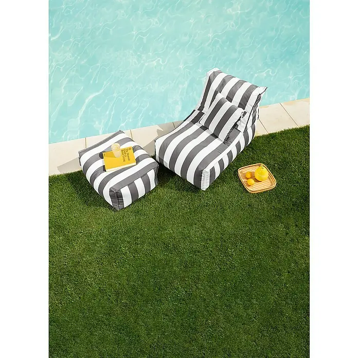 Sitting Point Sitzsack Santorin Rock - 100 x 65 x 65 cm, Anthrazit/Weiß, 100 % Polypropylen - Ein stilvolles Bild zeigt eine gestreifte Liege und einen Hocker am Pool, mit einem Buch und Getränken für entspannte Stunden.