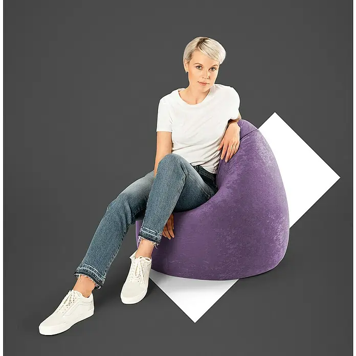 Sitting Point Sitzsack Beanbag Easy - XL, Lila, 100 % Polyester - Eine Frau sitzt auf einem violetten Sitzsack, gekleidet in Jeans und ein weißes T-Shirt, mit weißen Schuhen.