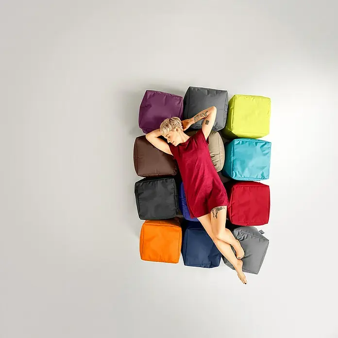 Sitting Point Sitzhocker Cube Scuba - 40 x 40 x 40 cm, Petrol, 100 % Polyester - Eine Frau entspannt sich auf einer Reihe von bunten Sitzwürfeln. Ideal für moderne Wohnräume und vielseitige Nutzung.