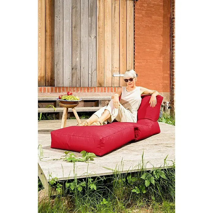 Sitting Point Sitzsack Twist Scuba - 90 x 70 x 80 cm, Rot, 100 % Polyester/100 % Polyvinylchlorid - Roter Lounge-Sessel im Freien mit einer Frau, die sich entspannt. Der Sessel hat ein Ottomane-Design und ist perfekt zum Entspannen im Garten.