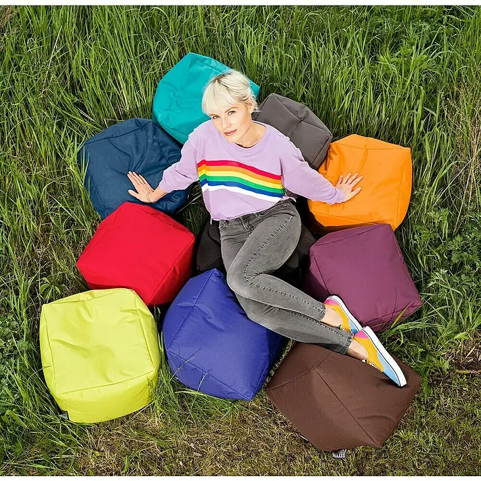 Sitting Point Sitzhocker Cube Scuba - 40 x 40 x 40 cm, Petrol, 100 % Polyester - Frau sitzt auf bunten Sitzwürfeln im Gras. Die Sitzwürfel sind in verschiedenen Farben erhältlich und bieten eine bequeme Sitzgelegenheit.