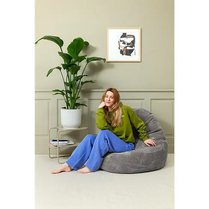 Sitzsack Beanbag Shara - XL, Anthrazit, 95 % Polyester, 5 % Nylon - Entspannung pur auf dem Cord-Sitzsack. Eine junge Frau macht es sich in einem grauen Sitzsack mit Cordbezug in einem gemütlichen Raum bequem.