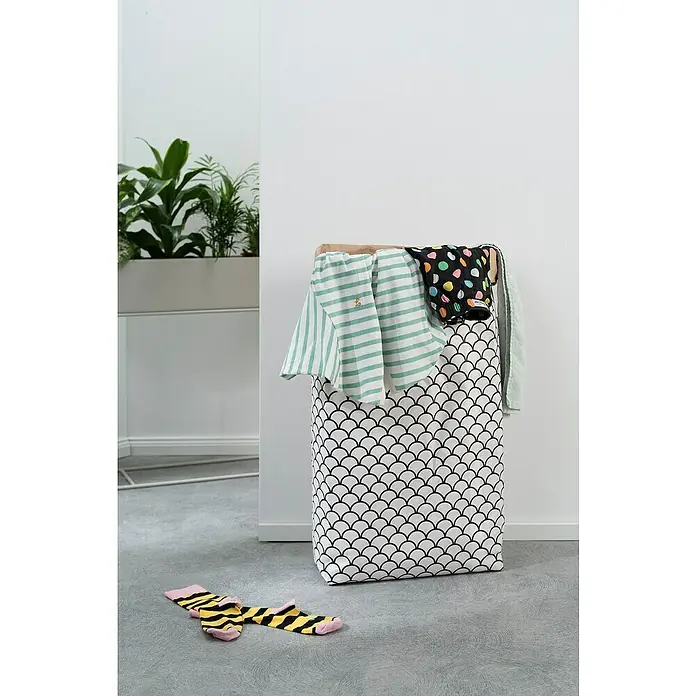 Sitting Point Polystyrolkugel Nachfüllpack - 60 l, Weiß - Wäschekorb mit Schuppenmuster gefüllt mit Kleidung, daneben liegen gestreifte Socken auf dem Boden. Praktische und stilvolle Aufbewahrung für Wäsche.