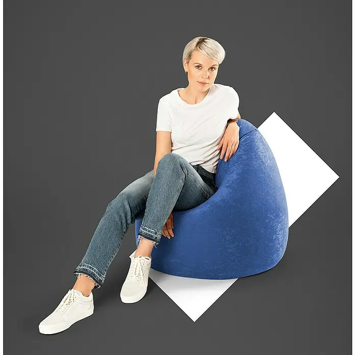 Sitting Point Sitzsack Beanbag EasyXL, Dunkelblau, 100 % Polyester - Eine Frau sitzt auf einem blauen Sitzsack vor einem grauen Hintergrund. Sie trägt Jeans, ein weißes T-Shirt und weiße Turnschuhe.