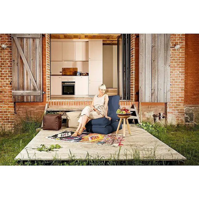 Sitting Point Sitzsack Twist Scuba - 90 x 70 x 80 cm, Jeansblau, 100 % Polyester - Eine Frau sitzt auf einem blauen Sitzsackstuhl im Freien. Der Sessel ist bequem und lädt zum Entspannen ein.