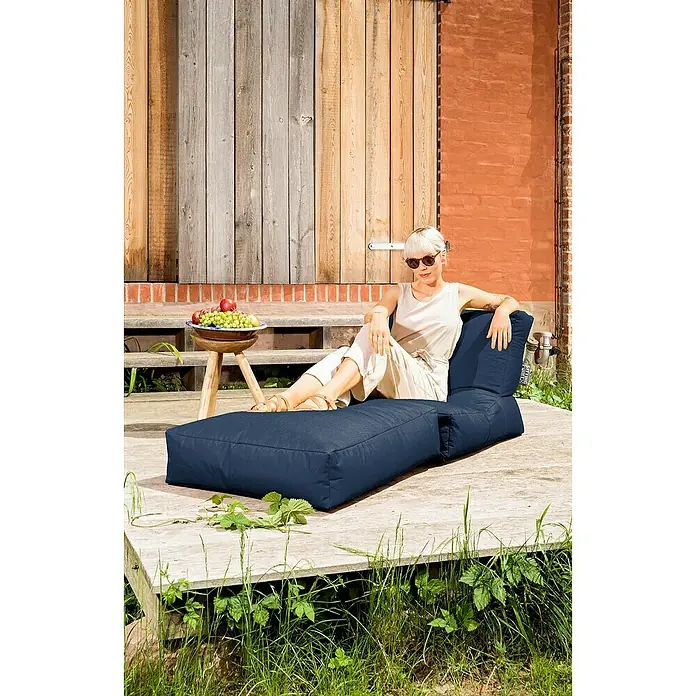 Sitting Point Sitzsack Twist Scuba - 90 x 70 x 80 cm, Jeansblau, 100 % Polyester - Eine Frau entspannt auf einem marineblauen Outdoor-Sitzsack-Sofa. Der Sitzsack bietet Komfort und Stil für entspannte Momente im Freien.