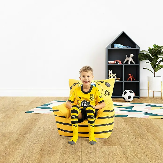 Sitting Point Sitzsack VIP Kids Sessel - 50 x 50 cm, BVB Emma, 100 % Polyester - Ein strahlender Junge im BVB-Outfit sitzt auf einem gelben BVB-Sitzsack, der mit Vereinslogo und Streifen verziert ist.