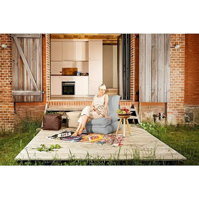 Sitting Point Sitzsack Twist Scuba - 90 x 70 x 80 cm, Grau, 100 % Polyester/100 % Polyvinylchlorid - Draußen entspannen: Eine Frau sitzt entspannt in einem grauen Sessel auf einer Terrasse, umgeben von üppigem Grün.