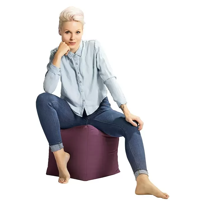 Sitting Point Sitzhocker Cube Scuba - 40 x 40 x 40 cm, Aubergine, 100 % Polyester - Frau sitzt auf einem lila Würfel-Ottoman, der seine Verwendung als bequemer Sitz demonstriert.