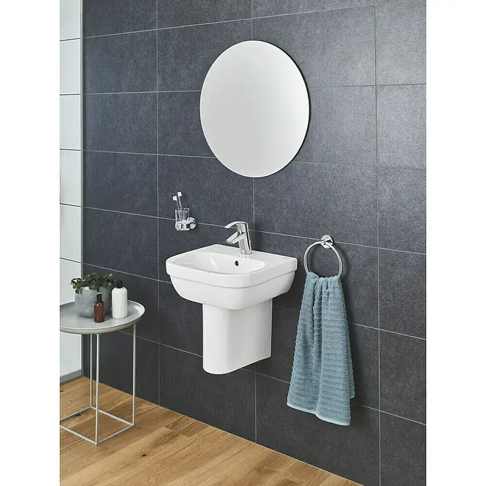Grohe Eurosmart Waschtischarmatur S-Size - Mit Zugstange, Chrom, Glänzend - Das Bild zeigt ein modernes Badezimmer mit einem weißen Waschbecken und einem runden Spiegel an einer grauen Wand.