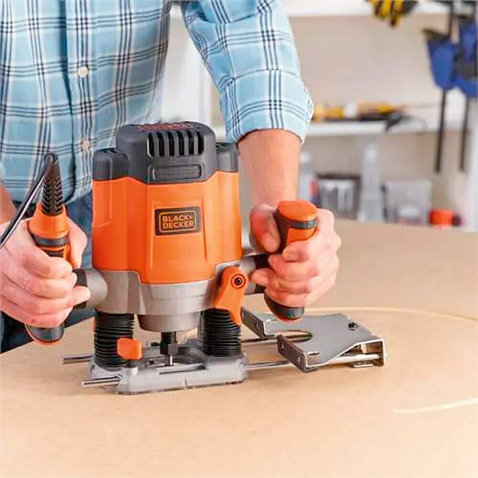Black+Decker Fresadora eléctrica KW1200EKA - 1.200 W, 8.000 r.p.m. - 28.000 r.p.m., Diámetro del portaherramientas: 38 mm - Un hombre usa una fresadora Black+Decker para dar forma a la madera con precisión. La herramienta asegura cortes limpios y profesionales en carpintería.