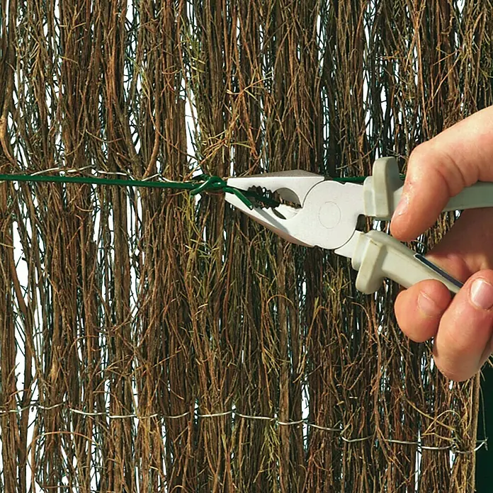 Alambre plastificado - Ø x L: 0,6 mm x 50 m - Primer plano de una persona que usa alicates para fijar alambre verde a una valla natural, mostrando la herramienta para una fijación segura.