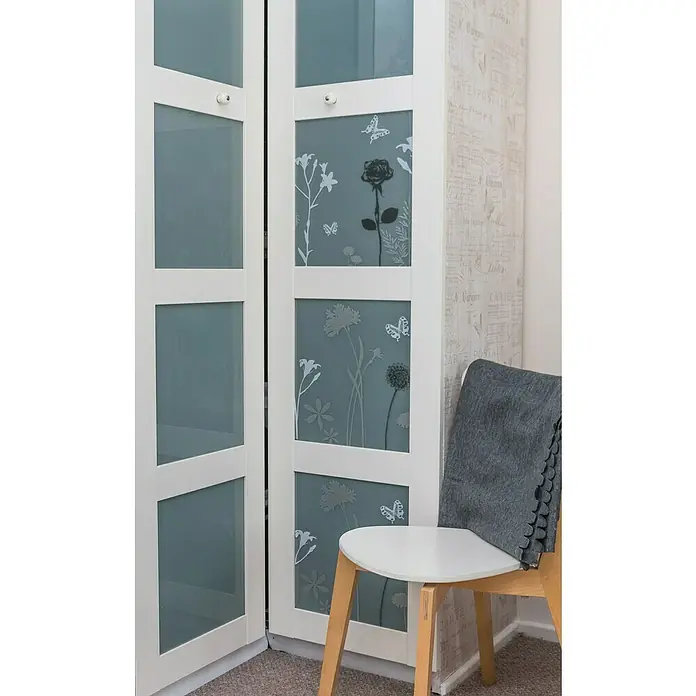 D-c-fix Static Premium Glasfolie Meterware Blossom - Breite: 45 cm, Transluzent, Statisch haftend - Ein weißer Schrank mit verzierten Glastüren steht neben einem Stuhl mit einer grauen Decke darauf.