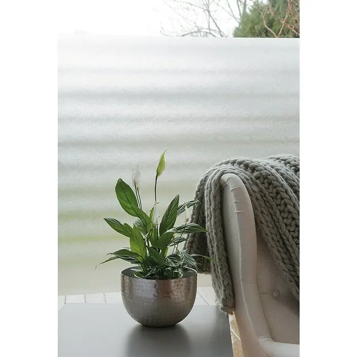 D-c-fix Static Premium Glasfolie Sofelto - 150 x 90 cm, Transluzent, Statisch haftend - Zimmerpflanze in einem silbernen Topf neben einer grauen Strickdecke auf einem Sessel vor einem Fenster, das ein ruhiges, gemütliches Ambiente schafft.