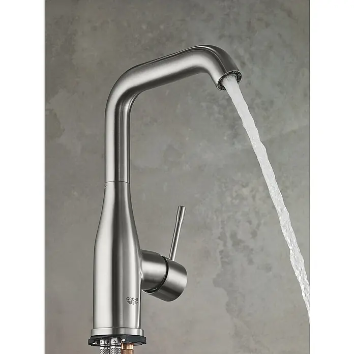 Grohe Essence New Waschtischarmatur L-Size - Mit Zugstange, Supersteel, Glänzend - Nahaufnahme eines Grohe Wasserhahns aus gebürstetem Nickel mit fließendem Wasser vor einem grauen Hintergrund.