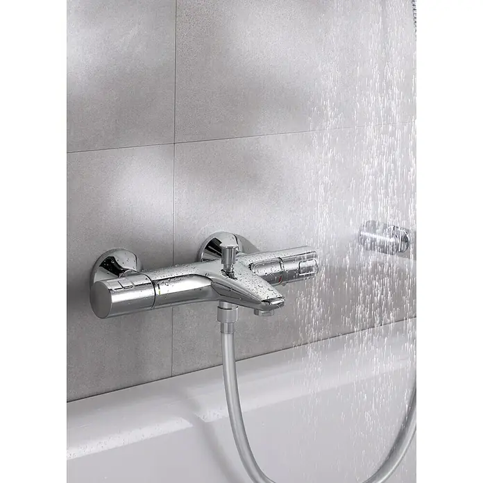 Grohe QuickFix Grifo termostático de bañera Precision Start - Cromo - Primer plano de un brillante grifo de ducha cromado montado en una pared de azulejos grises con agua que sale del cabezal de la ducha.