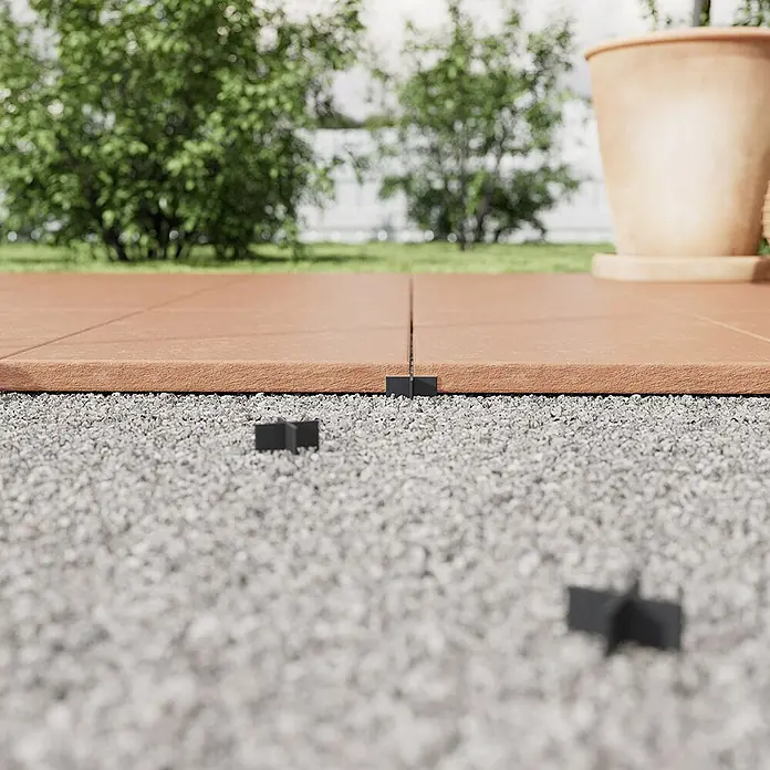 Langfit Fugenkreuz - 100 Stk., Fugenbreite 6 mm - Nahaufnahme von braunen Terrassenfliesen, die mit schwarzen Abstandshaltern auf Kies verlegt sind.