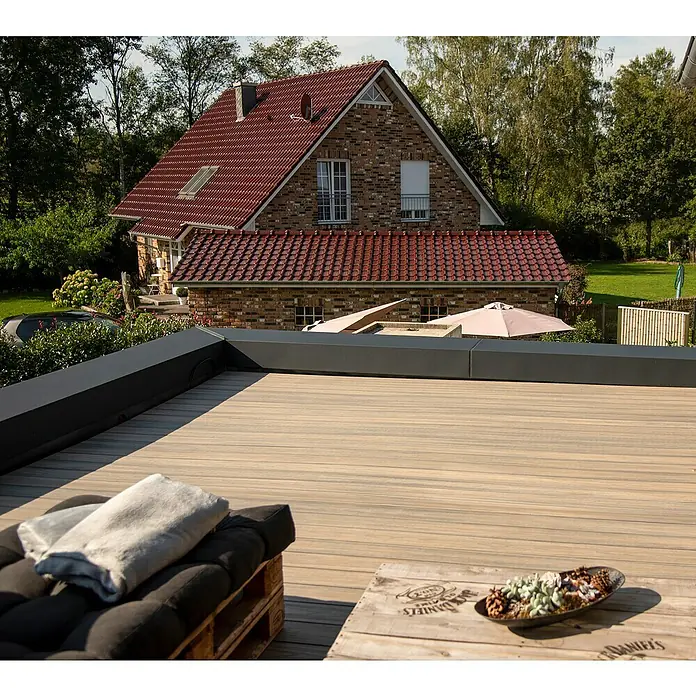 Elephant Terrassenbau-Set WPC strongWood - Muschel/Stein, Deckfläche pro Paket: 12 m² - Einladende Holzterrasse mit stilvollem Palettenmöbel und dekorativer Schale, vor dem Hintergrund eines charmanten Hauses.