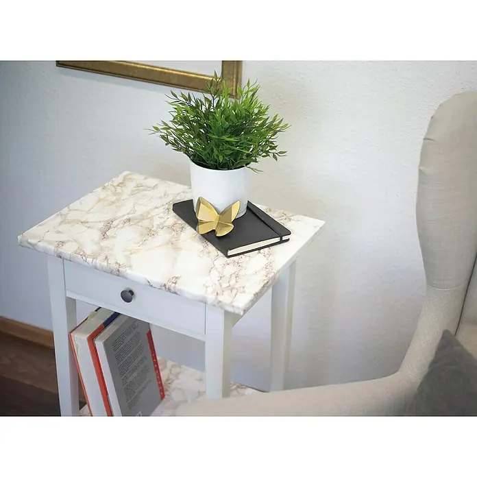 D-c-fix Marmoreffektfolie Cortes - 200 x 67,5 cm, Braun, Selbstklebend - Ein Marmor-Beistelltisch mit einer grünen Pflanze, einem Notizbuch und einem goldenen Schmetterling darauf, neben einem beigen Sessel.
