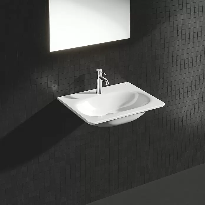 Grohe Essence New Waschtischarmatur S-Size - Mit Zugstange, Chrom, Glänzend - Weißes Keramik-Wandwaschbecken mit Chromarmatur in einem modernen Bad mit dunklen Fliesen.