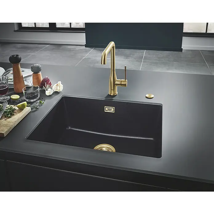 Grohe Essence Spültischarmatur - U-Auslauf, Cool Sunrise, Matt - Schwarze Küchenspüle mit goldener Armatur und einigen Lebensmitteln auf der Arbeitsplatte.