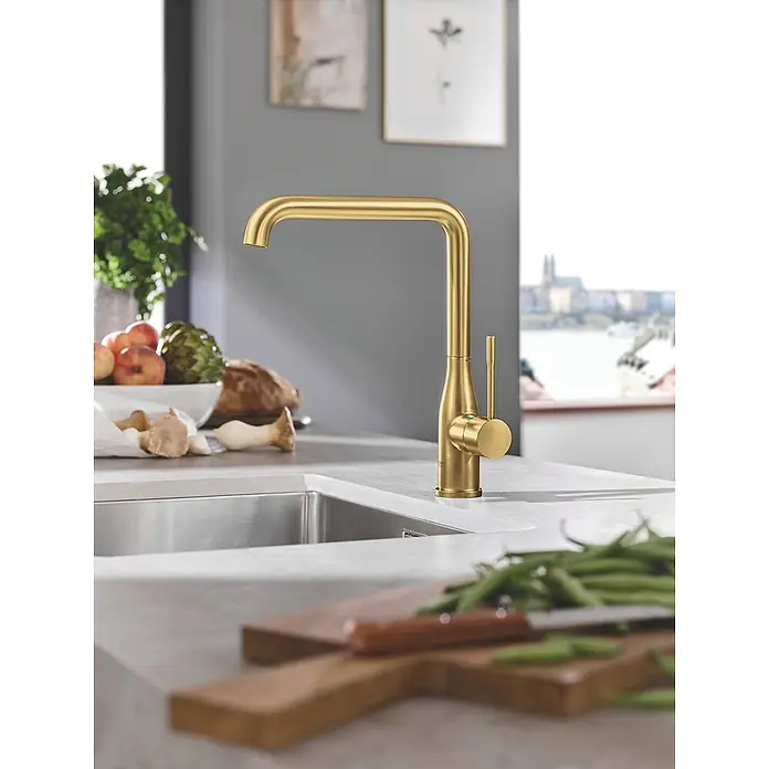 Grohe Essence Spültischarmatur - U-Auslauf, Cool Sunrise, Matt - Goldener Wasserhahn auf einer Küchentheke, umgeben von frischen Zutaten, die eine elegante und funktionale Küchenarmatur hervorheben.