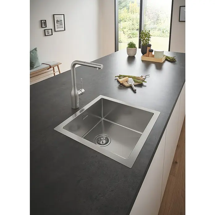 Grohe Essence Spültischarmatur - L-Auslauf, Supersteel, Matt - Ein moderner Edelstahlspültisch mit einer Armatur, eingebettet in eine dunkle Arbeitsplatte, präsentiert die elegante Funktionalität des Küchenbereichs.