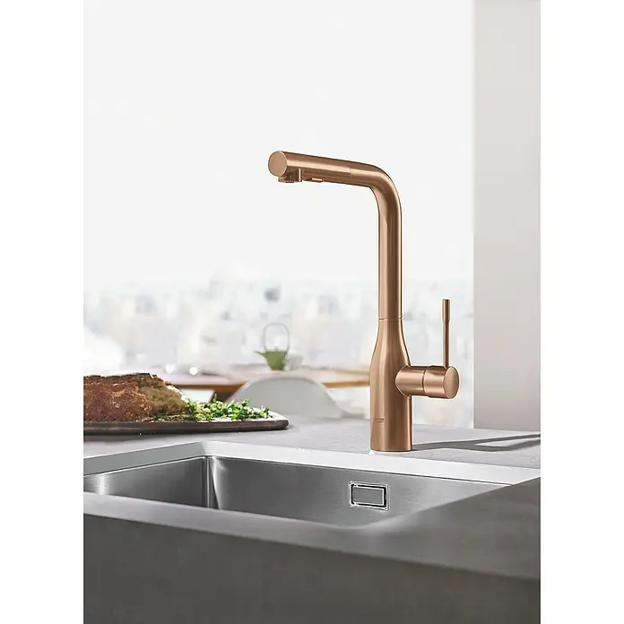 Grohe Essence Spültischarmatur - L-Auslauf, Warm Sunset, Matt - Nahaufnahme eines GROHE Essence Küchenarmatur in gebürstetem Roségold vor einer hellen Küche.