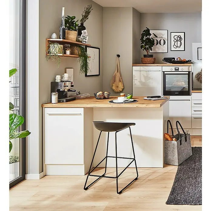 Respekta Inselküche Gabriel - Breite: 150 cm, Weiß, Ohne Elektrogeräte - Das Bild zeigt eine moderne Küche mit einem schwarzen Barhocker, der das minimalistische Design ergänzt. Die Holzarbeitsplatte und die Pflanzen bringen Wärme in den Raum.