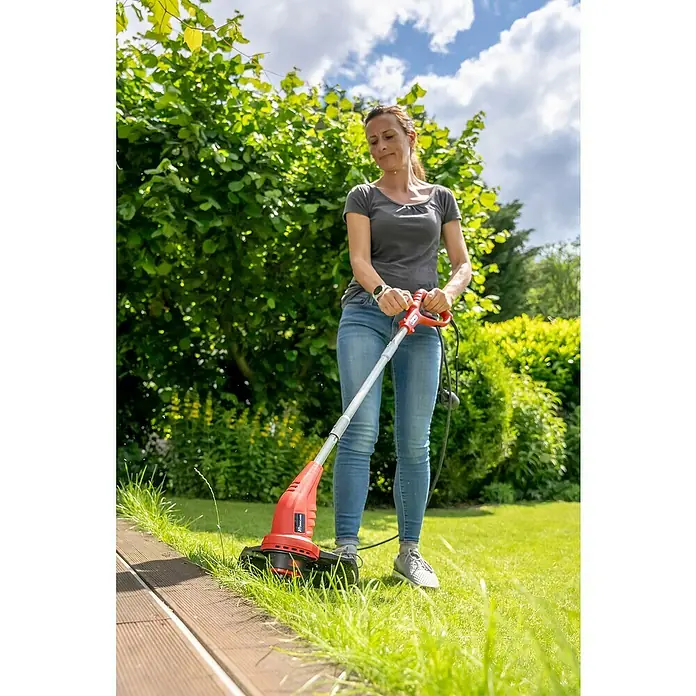 Hurricane Elektro-Rasentrimmer HERT-I-3025 - 300 W, Schnittbreite Faden: 25 cm - Eine Frau benutzt einen Rasentrimmer, um den Rasen zu schneiden. Der Trimmer ist rot und schwarz und hat einen Teleskopstiel.