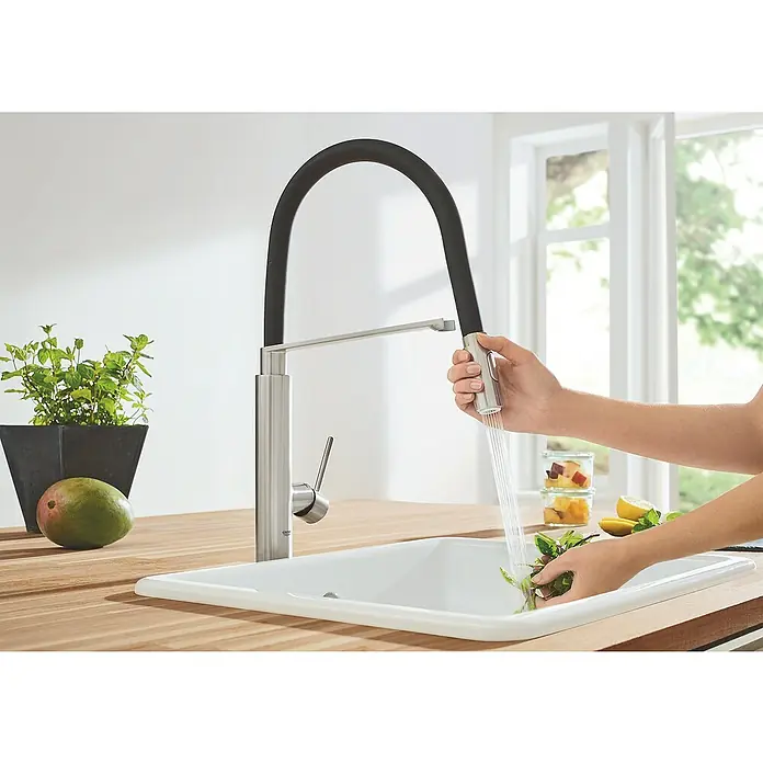 Grohe Concetto Spültischarmatur - Supersteel/Schwarz, Matt - Diese Nahaufnahme zeigt eine elegante Spültischarmatur in Aktion, während sie frische Kräuter unter fließendem Wasser reinigt.