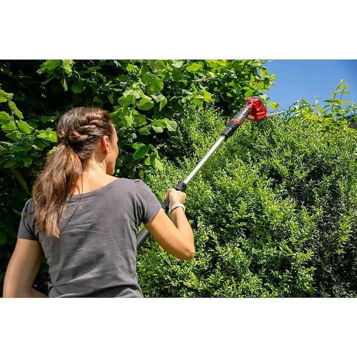 Hurricane Akku-Gras- & Strauchschere HGS-I-120 - 12 V, Li-Ionen, 1 Akku - Frau schneidet eine Hecke mit einer Akku-Heckenschere mit Teleskopstiel. Das Produkt ist perfekt für Gartenarbeiten.