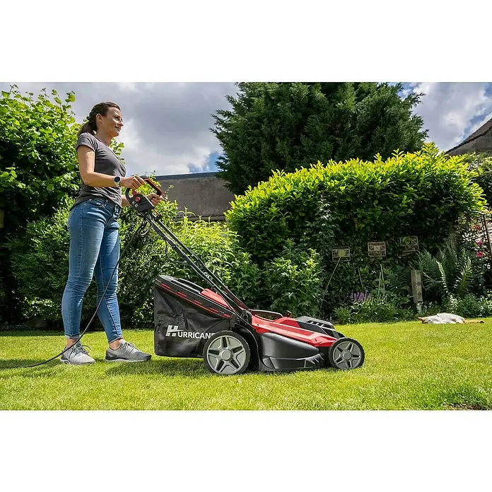 Hurricane Elektro-Rasenmäher HERM-I-1743 - 1.700 W, Schnittbreite: 43 cm - Eine Frau benutzt einen HURRICANE Rasenmäher im Garten, um das Gras zu schneiden. Das Gerät ist rot und schwarz.