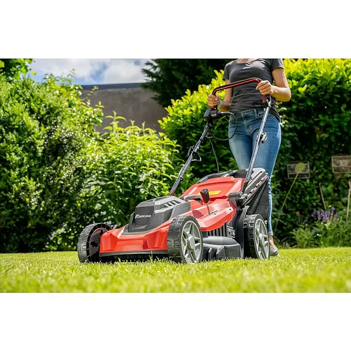 Hurricane Elektro-Rasenmäher HERM-I-1743 - 1.700 W, Schnittbreite: 43 cm - Rasenmäher Hurricane im Einsatz: Eine Frau mäht den Rasen mit einem roten Hurricane-Rasenmäher im Garten, umgeben von Grün.