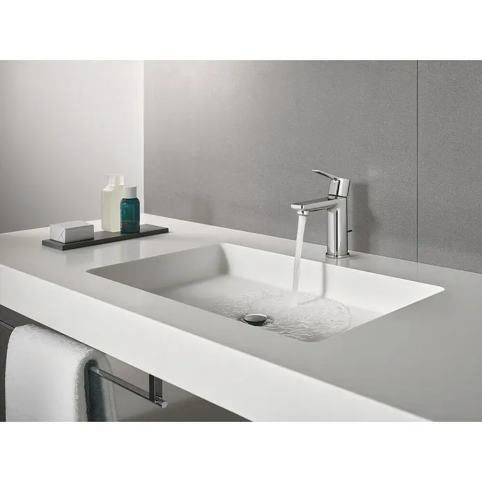 Grohe Lineare Waschtischarmatur XS-Size - Mit Zugstange, Chrom, Glänzend - Ein modernes Waschbecken mit einem eleganten Chromhahn, aus dem Wasser fließt, und Ablagefläche mit Seife und Lotionen.