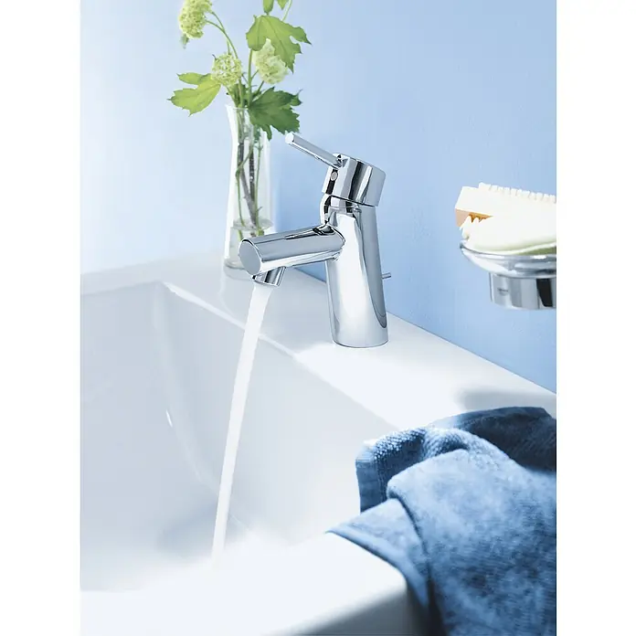 Grohe Concetto Waschtischarmatur S-Size - Mit Zugstange, Chrom, Glänzend - Dieses Bild zeigt einen glänzenden, modernen Wasserhahn mit fließendem Wasser in einem stilvollen Badezimmerambiente.