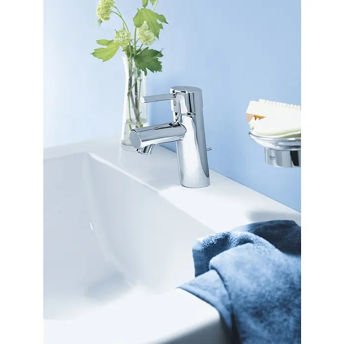Grohe Concetto Waschtischarmatur S-Size - Mit Zugstange, Chrom, Glänzend - Bild einer modernen Chromarmatur von Grohe auf einem weißen Waschbecken, ergänzt durch eine Vase mit Blumen und ein blaues Handtuch.