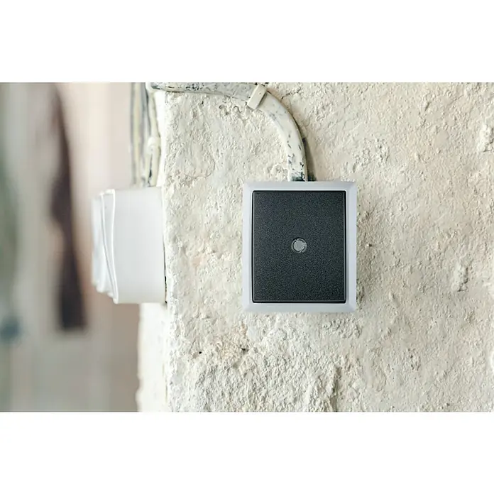 Aqua Form Feuchtraum-Kontrollschalter - Anthrazit, Aufputzmontage, IP44 - Nahaufnahme eines modernen, quadratischen Lichtschalters mit grauer Taste und weißem Rahmen, montiert auf einer grob verputzten Wand.