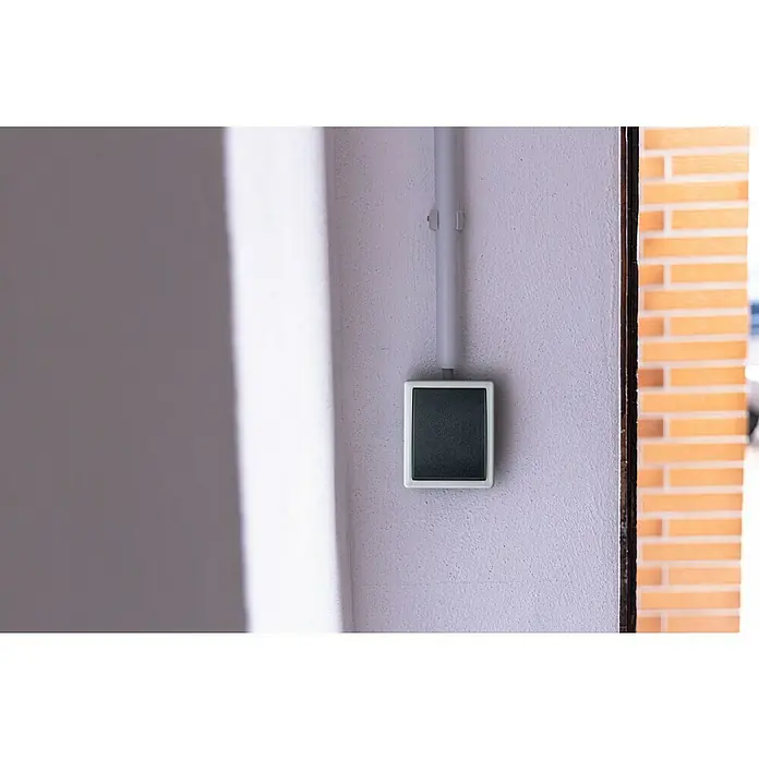 Aqua Form Feuchtraumtaster - Anthrazit, Aufputzmontage, IP44 - Nahaufnahme einer quadratischen, schwarzen Türklingel mit weißer Umrandung, die an einer hellen Wand befestigt ist.