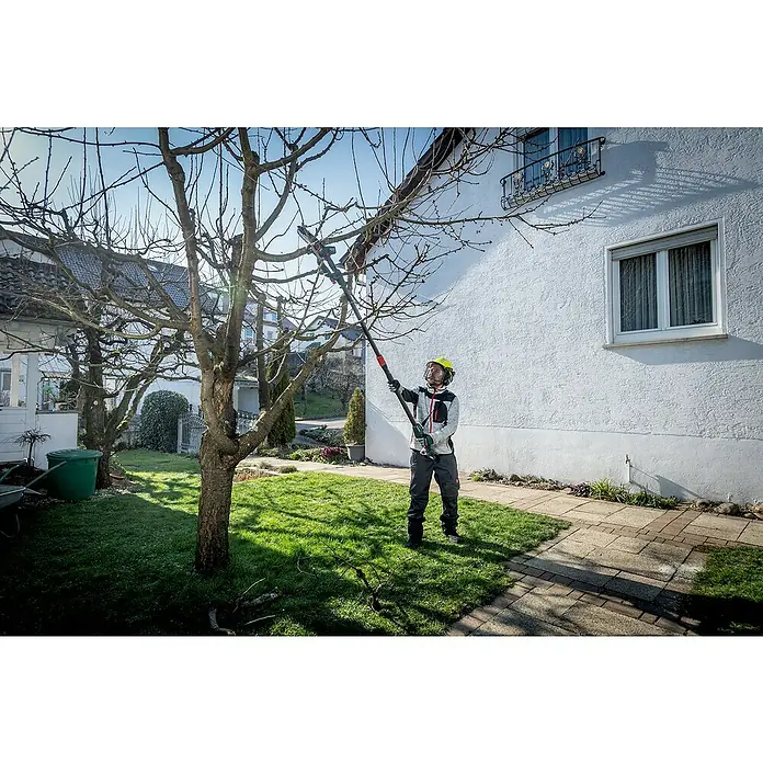 Metabo Teleskopstab MS - Passend für: Akku-Gehölzsäge MS 18 LTX 15 - Eine Person mit Schutzhelm schneidet mit einer Kettensäge Äste eines Baumes in einem Garten. Das Werkzeug ermöglicht sicheres Arbeiten in der Höhe.