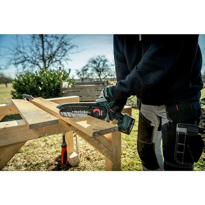 Metabo CAS 18V Einhand-Akku-Kettensäge MS 18 LTX 15 mit Werkzeugtasche - 18 V, 2 Ah, Li-Ionen - Nahaufnahme einer Person, die mit einer Metabo Akku-Kettensäge ein Holzbrett auf einem Holzbock zuschneidet.
