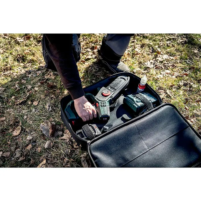 Metabo CAS 18V Einhand-Akku-Kettensäge MS 18 LTX 15 mit Werkzeugtasche - 18 V, 2 Ah, Li-Ionen - Ein Mann nimmt eine Metabo Akku-Kettensäge aus einer schwarzen Tragetasche im Freien, mit Akku und Ölflasche.