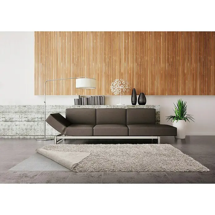 D-c-fix Teppichgleitschutz Comfort - 120 x 60 cm, Selbstklebend - Ein grauer, hochfloriger Teppich liegt in einem modern eingerichteten Wohnzimmer mit braunem Sofa und Holzwand.