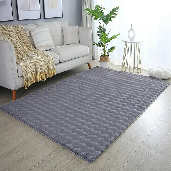 Fellteppich Ambiance - Grau, 150 x 80 cm, 100 % Polyester - Ein grauer, strukturierter Teppich liegt im Wohnzimmer vor einem Sofa, einem Beistelltisch und einer Pflanze.